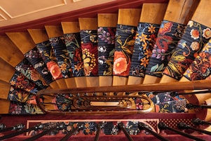 Una scala a chiocciola con tappeti decorati a motivi floreali e una ringhiera centrale.
