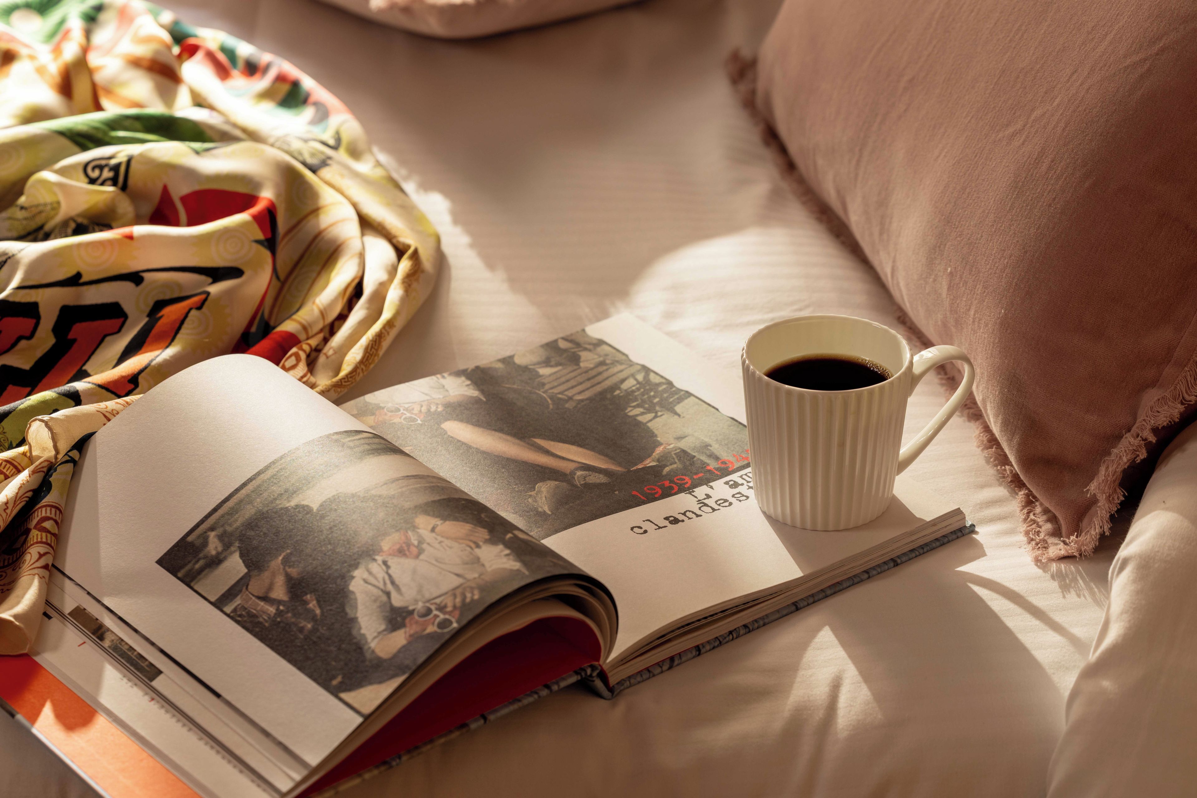 Un livre, une tasse de café et un oreiller sur un lit.