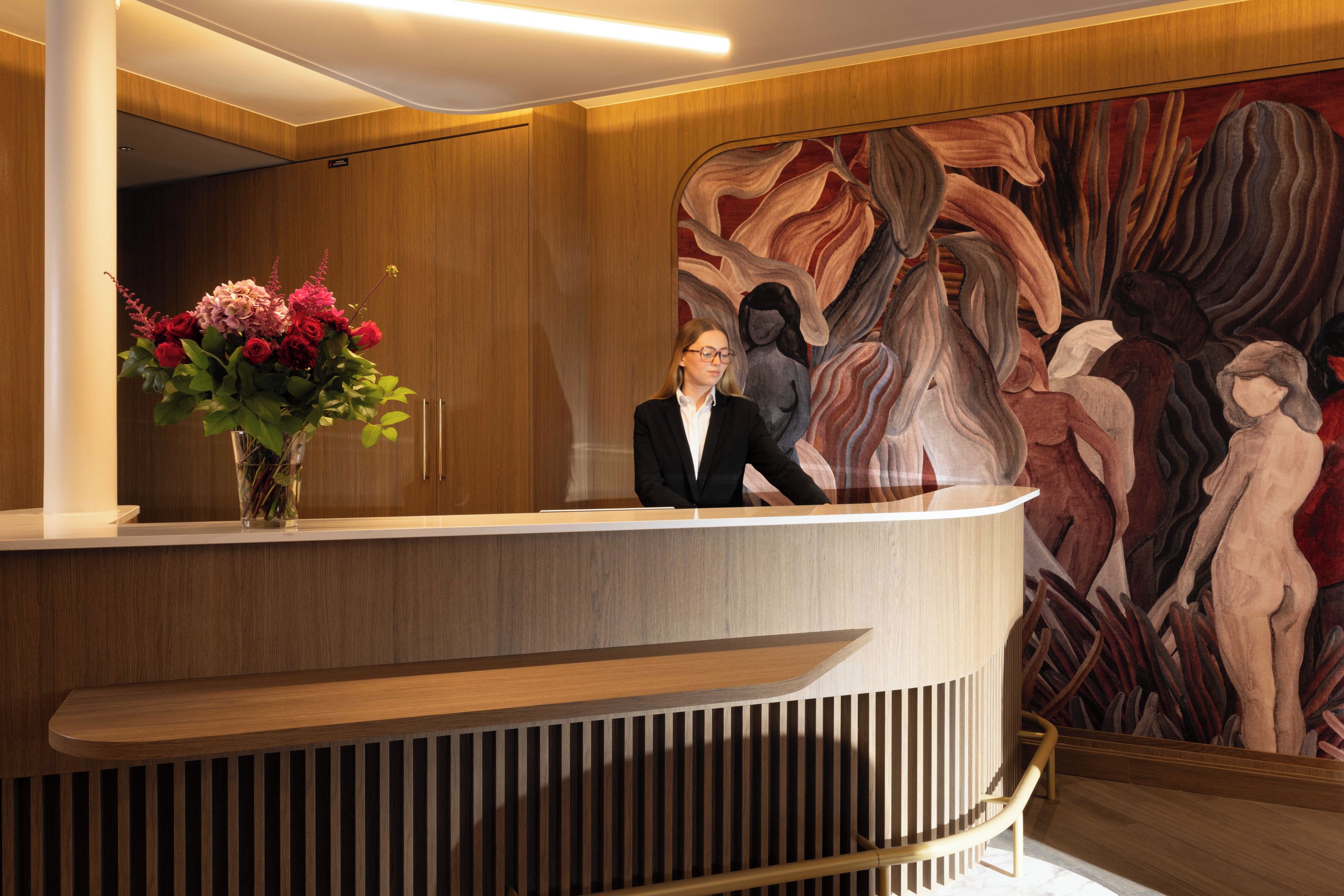 A reception desk with a vase of flowers, a wooden panel wall, and a large abstract painting.