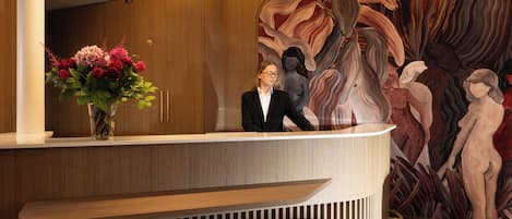 A reception desk with a vase of flowers, a wooden panel wall, and a large abstract painting.