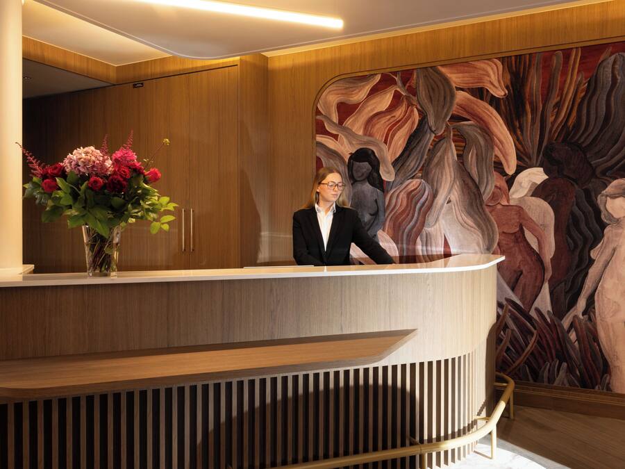 A reception desk with a vase of flowers, a wooden panel wall, and a large abstract painting.