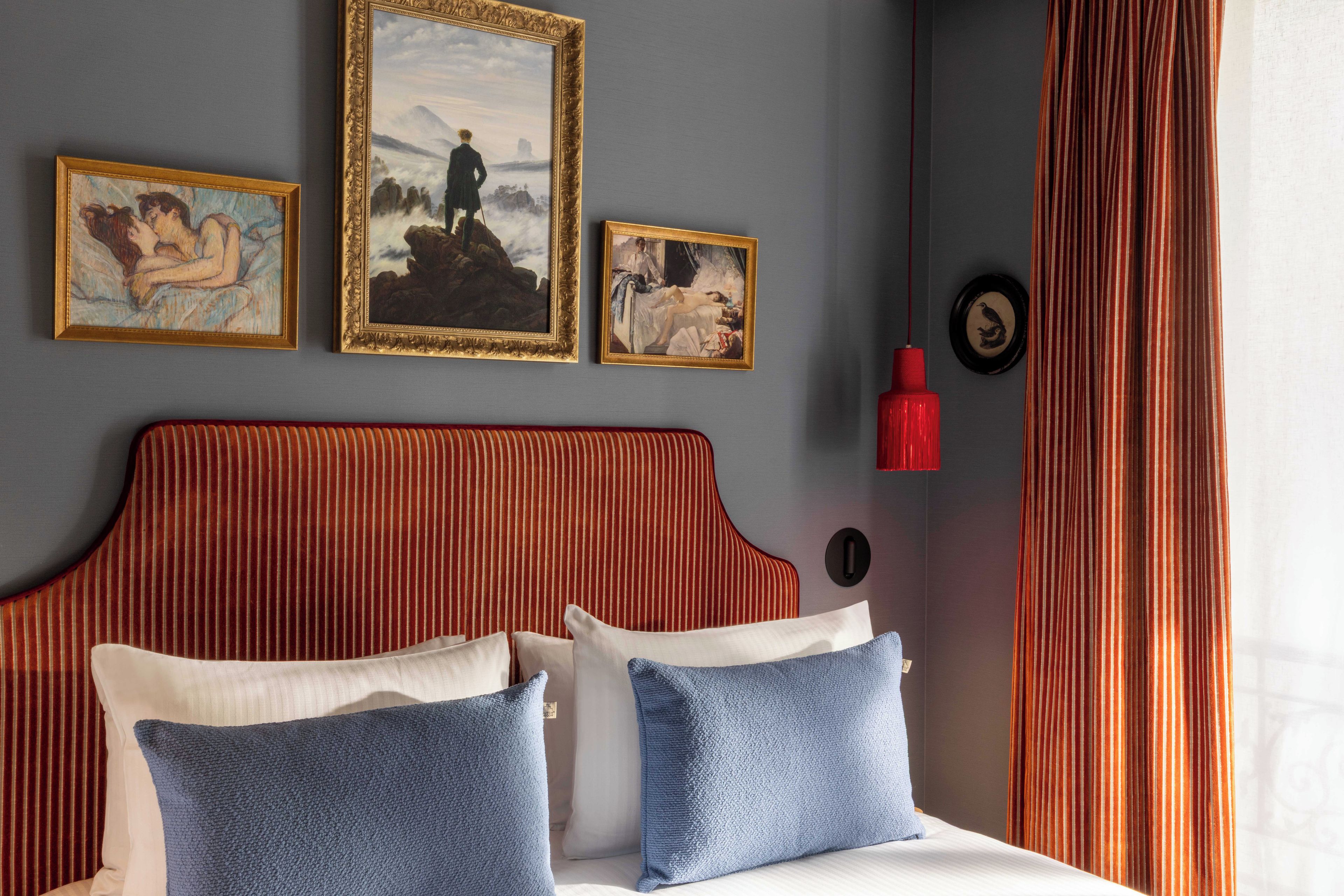 A hotel room with a large bed, two pillows, a headboard, and three framed artworks on the wall.