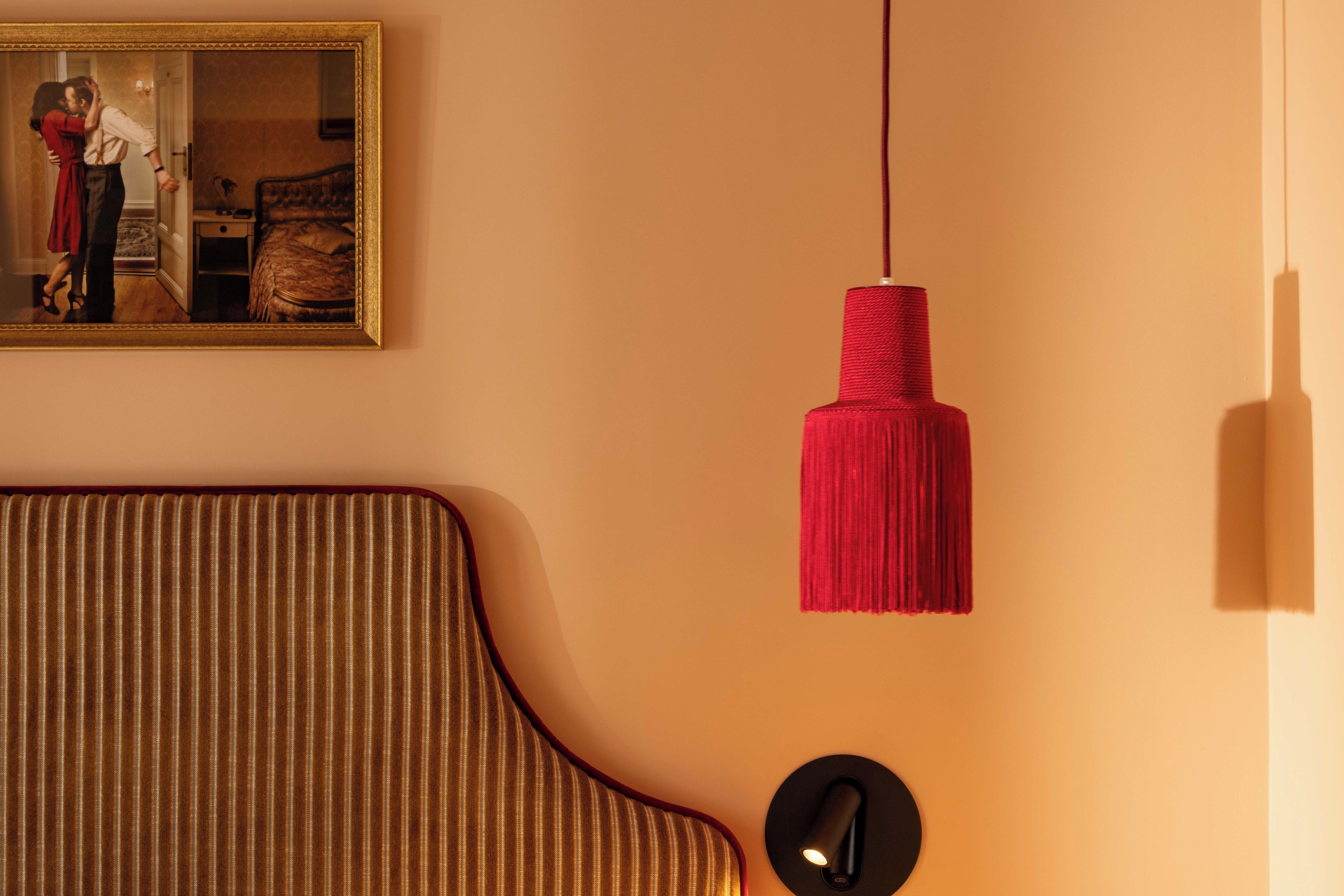 Una habitación con un sofá, una lámpara colgante roja y un espejo enmarco que refleja a una persona.