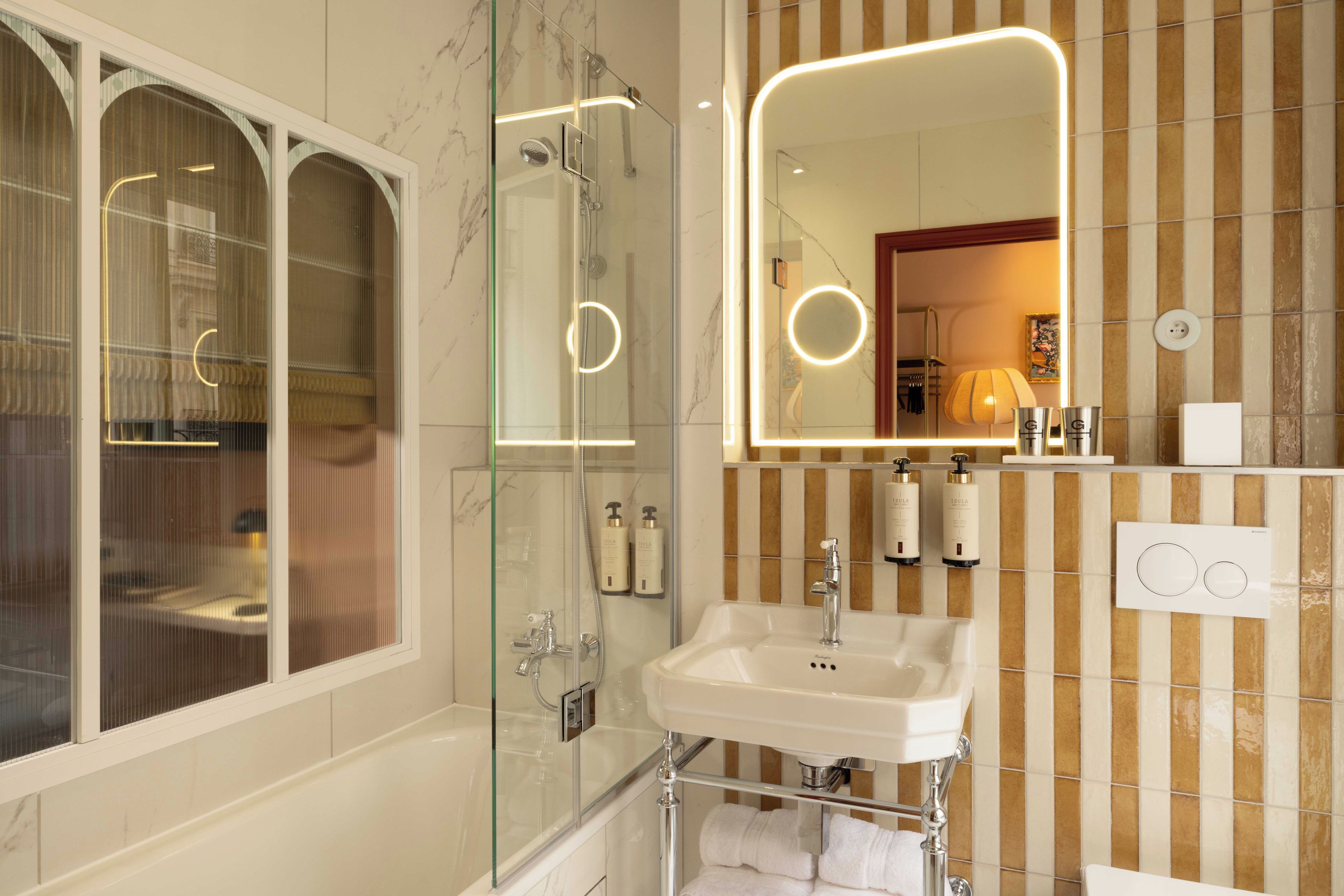 A bathroom with a glass-enclosed shower, a sink with a mirror, and toiletries on the wall.