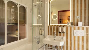 A bathroom with a glass-enclosed shower, a sink with a mirror, and toiletries on the wall.