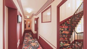 A hallway with a floral carpet, a staircase with patterned steps, and a door with a mirror. - Grand Hotel De Turin (Paris)