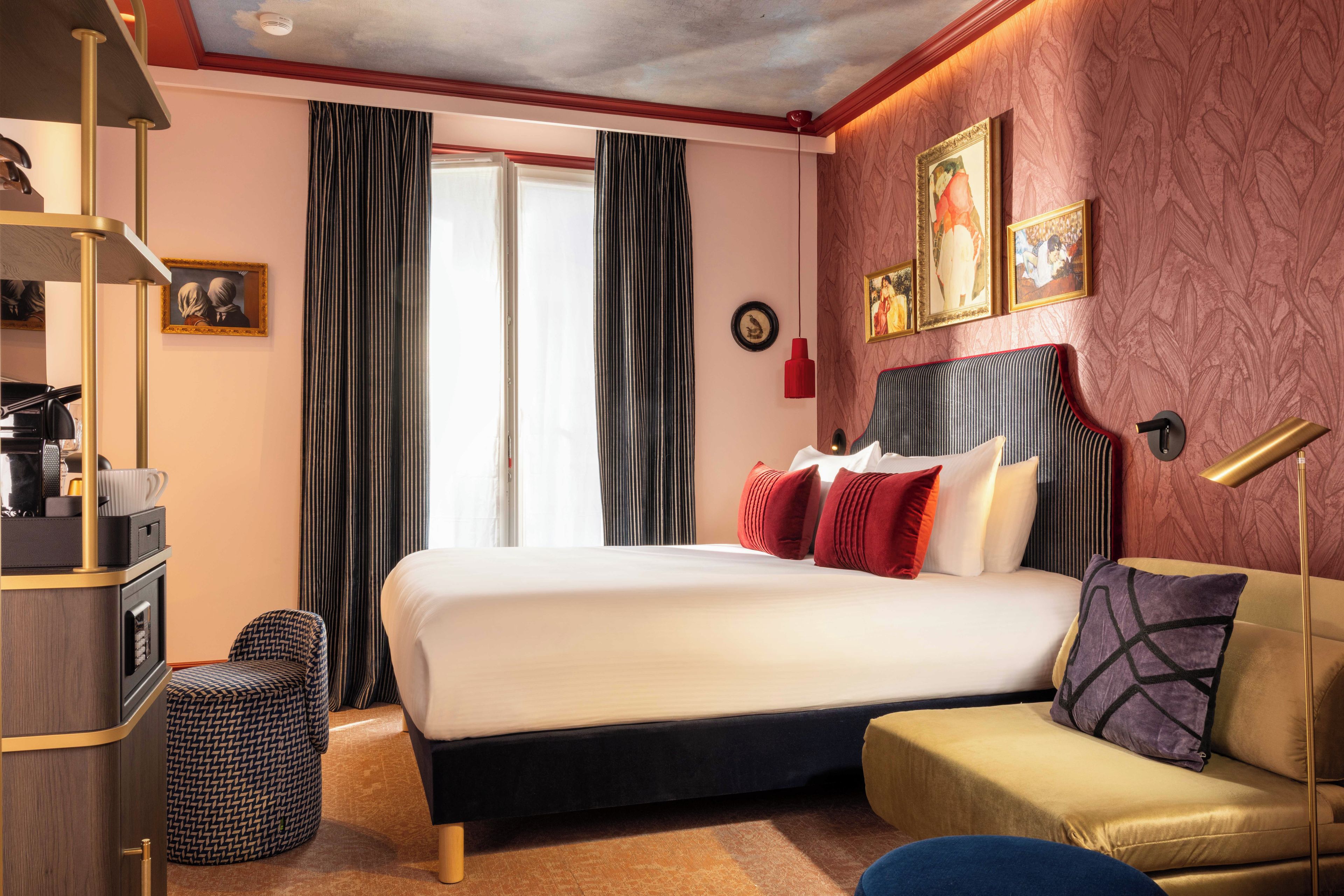 Habitación de hotel con cama, sofá, escritorio y silla. Hay cortinas, un reloj y cuadros en la pared.