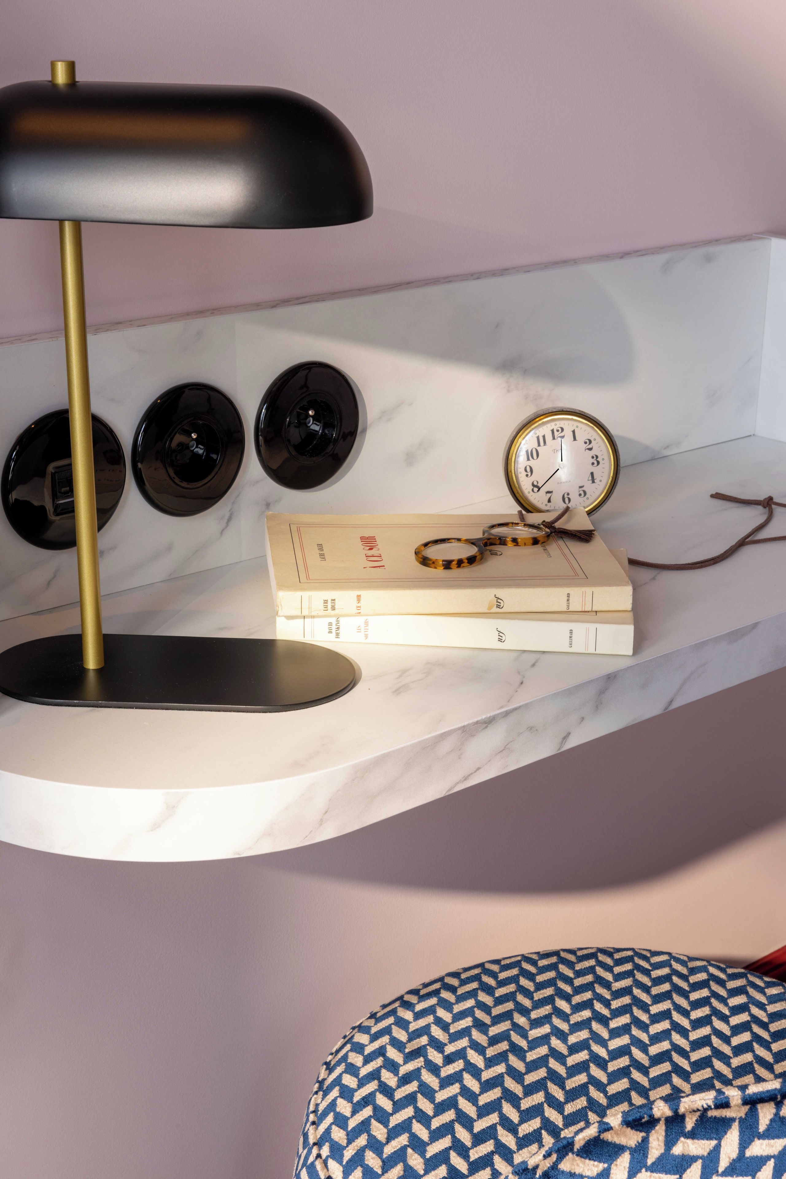 Una scrivania moderna con una lampada nera, un orologio e libri su una mensola in marmo.