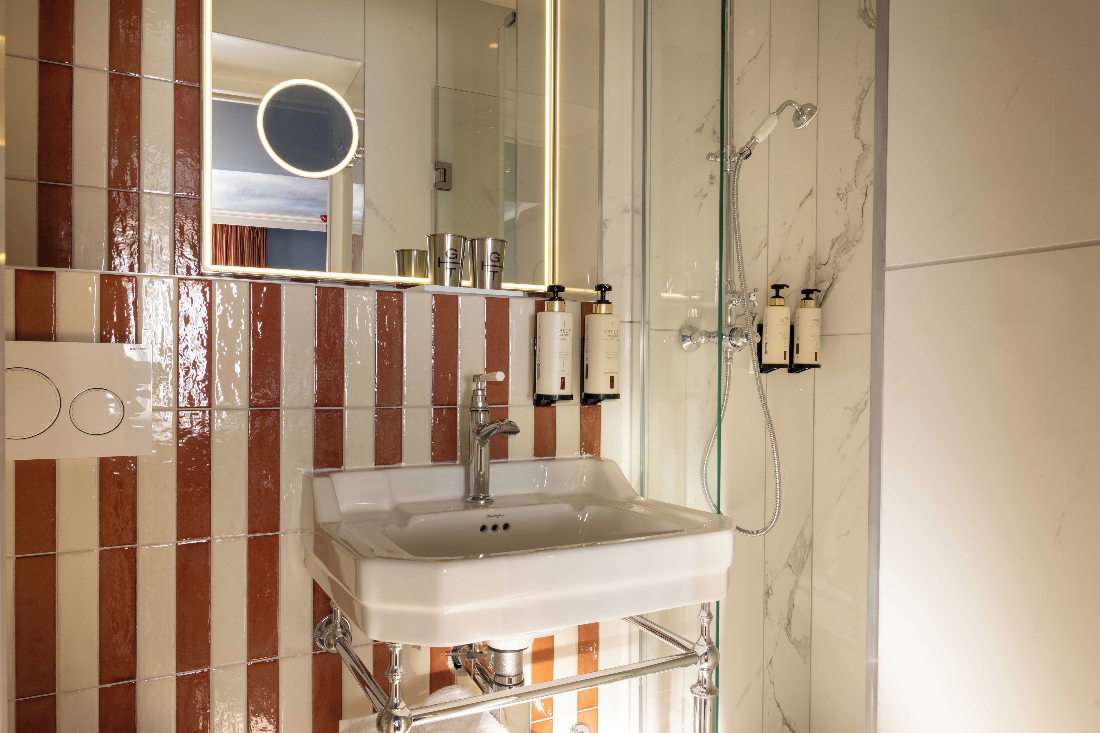 A bathroom with a white sink, a glass shower enclosure, and a mirror with a round frame.