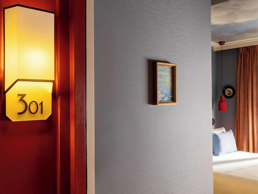 A hotel room with a number sign, a framed picture, and a bed with curtains.