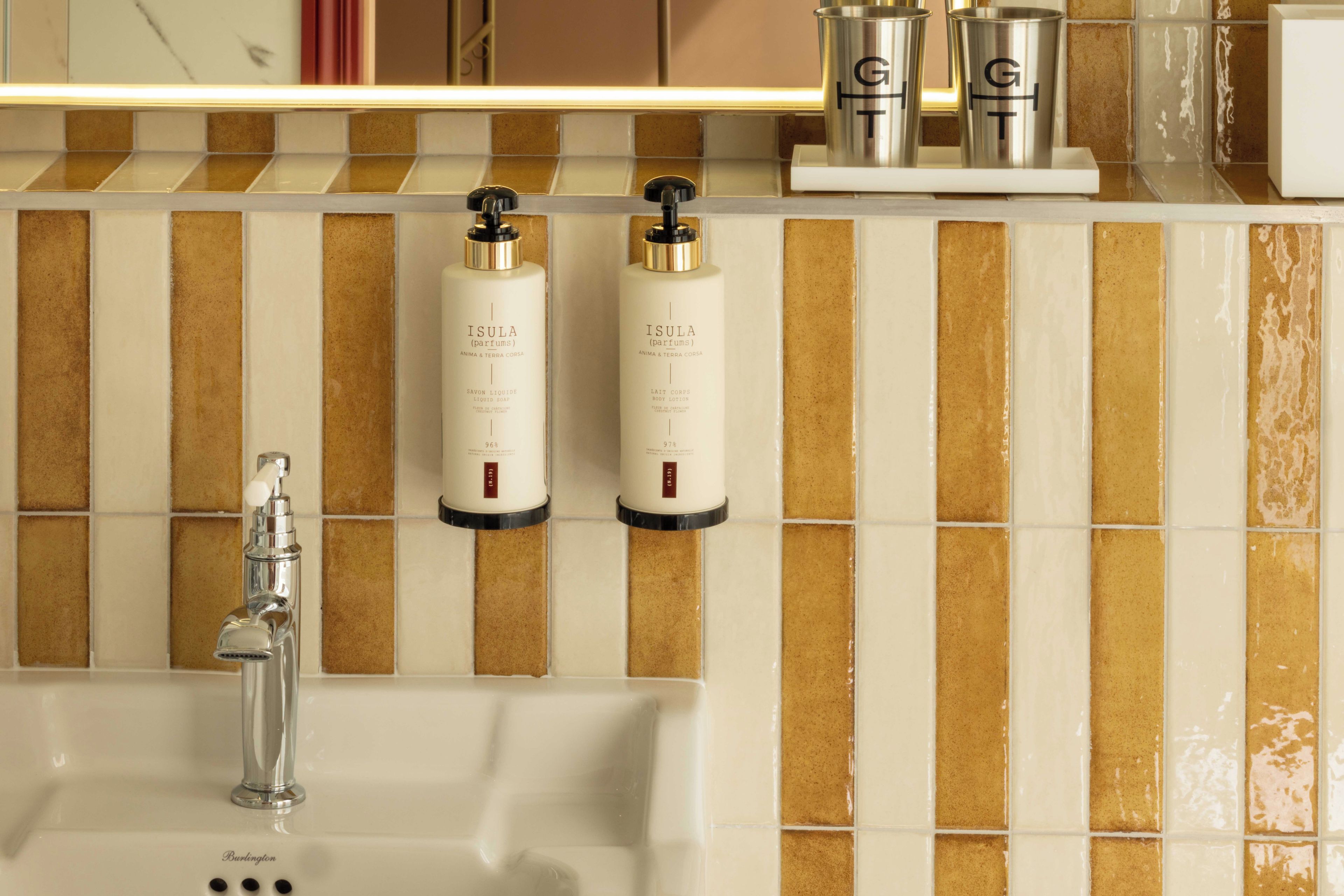 A bathroom with a white sink, two bottles of Isula body lotion, and a faucet.