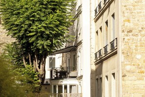 A narrow street with a tree on the left and a building with balconies on the right. - Grand Hotel De Turin (Paris)