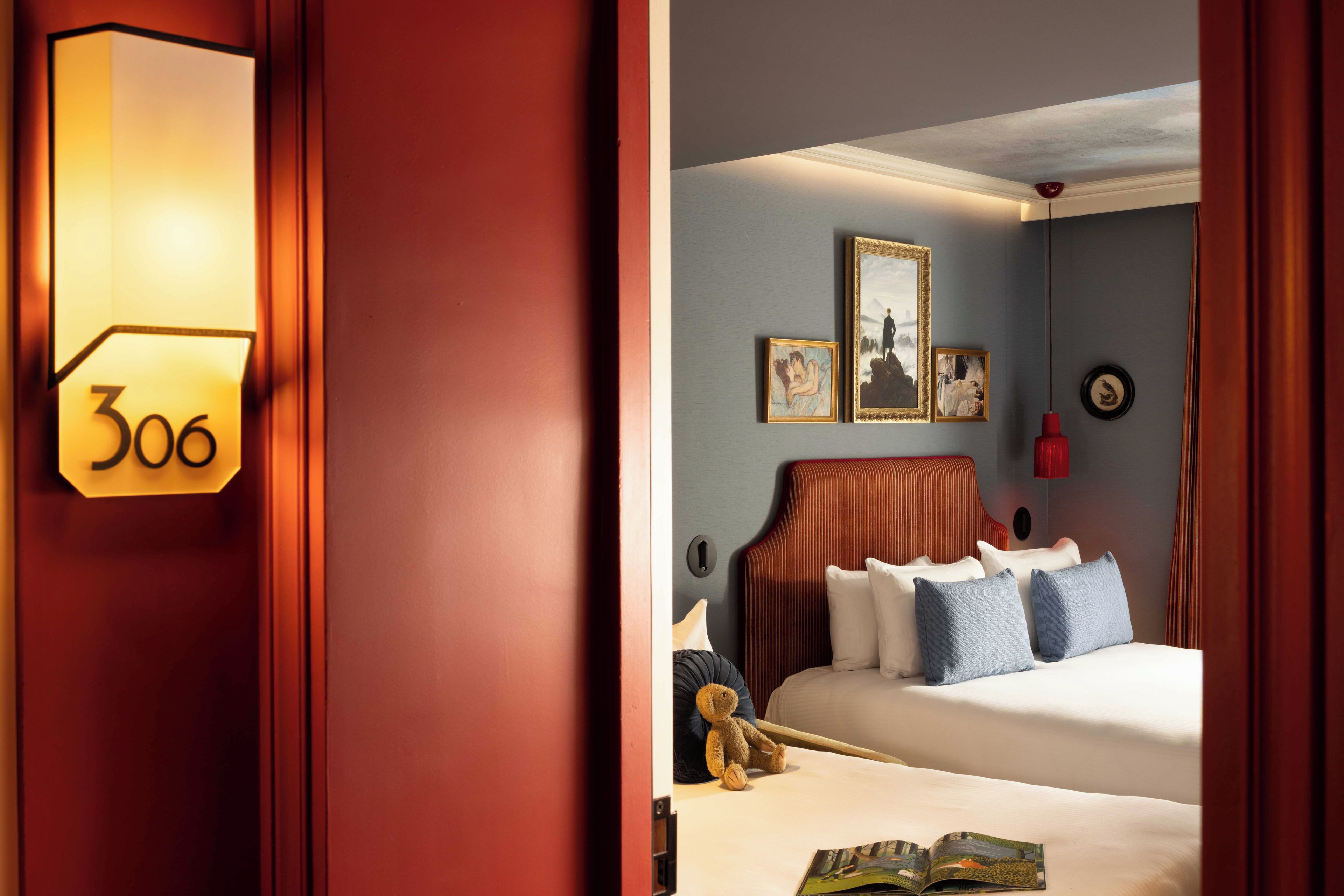 Een hotelkamer met een groot bed, een nachtkastje, een teddybeer en een wandlamp.