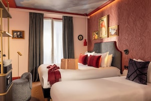 Habitación de hotel con dos camas, un escritorio y una silla. Hay cortinas, un cuadro y un reloj en la pared.