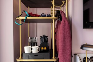 A room with a gold-framed shelf unit containing a kettle, two cups, and a small black box.