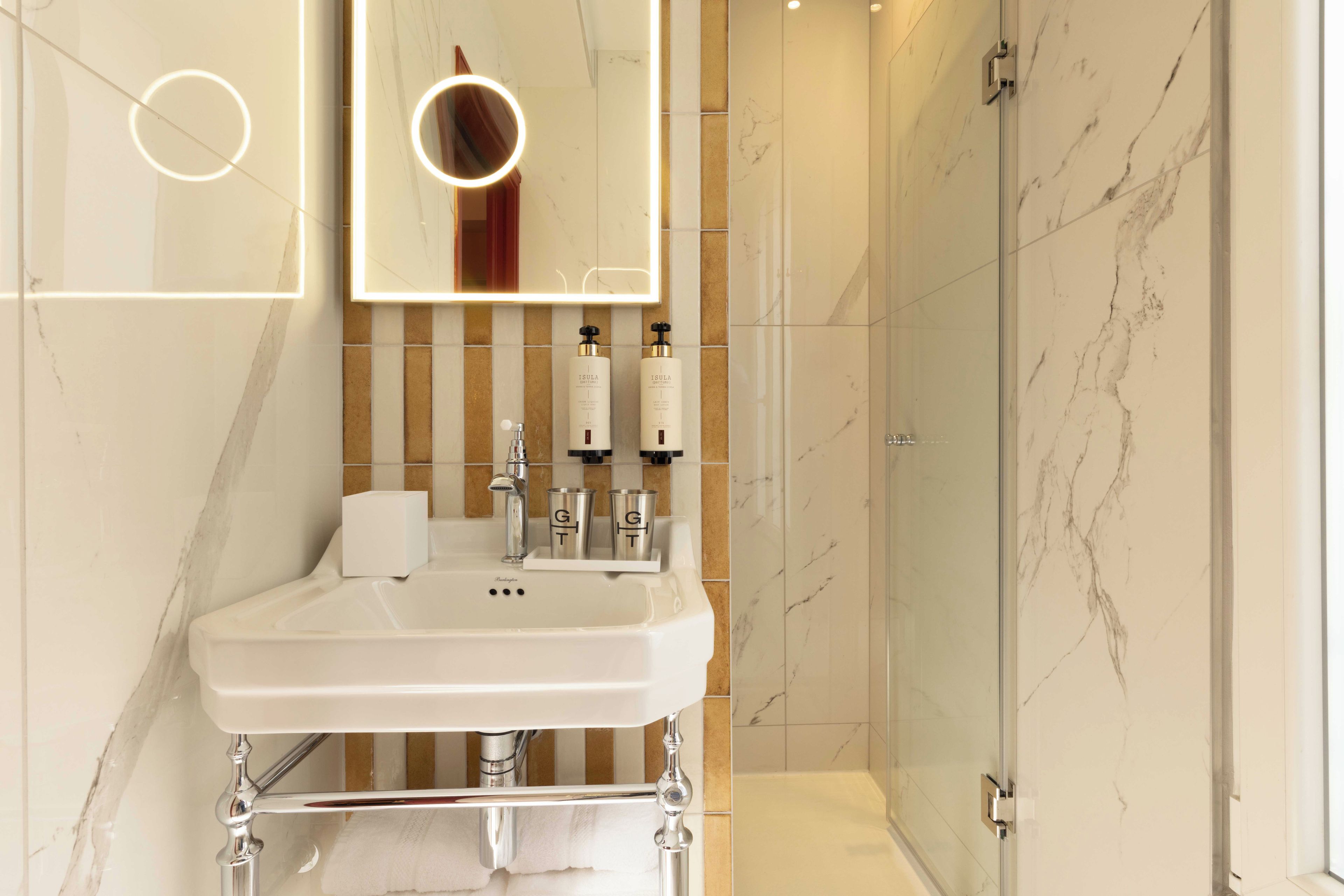 Un baño moderno con un lavabo blanco, dos espejos y una cabina de ducha con mampara de vidrio.