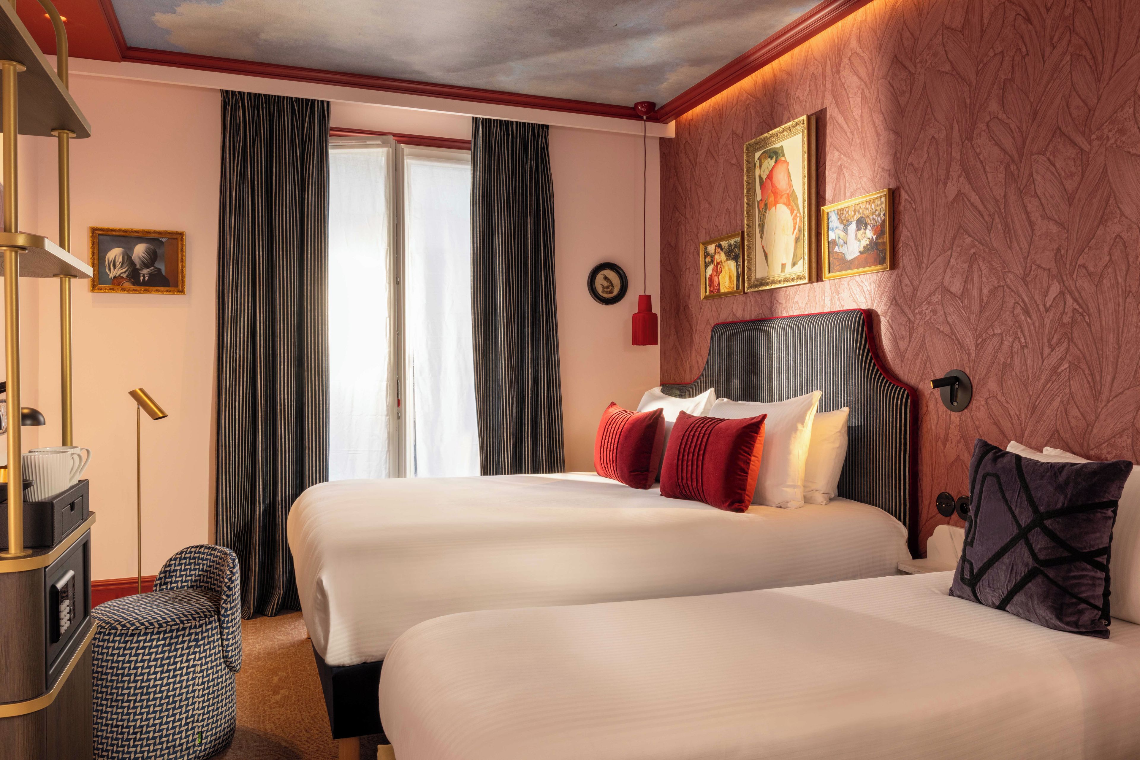 A hotel room with two beds, a desk, a chair, and a large window with curtains.