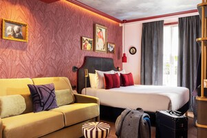 A hotel room with a bed, a sofa, a small round ottoman, and a suitcase.