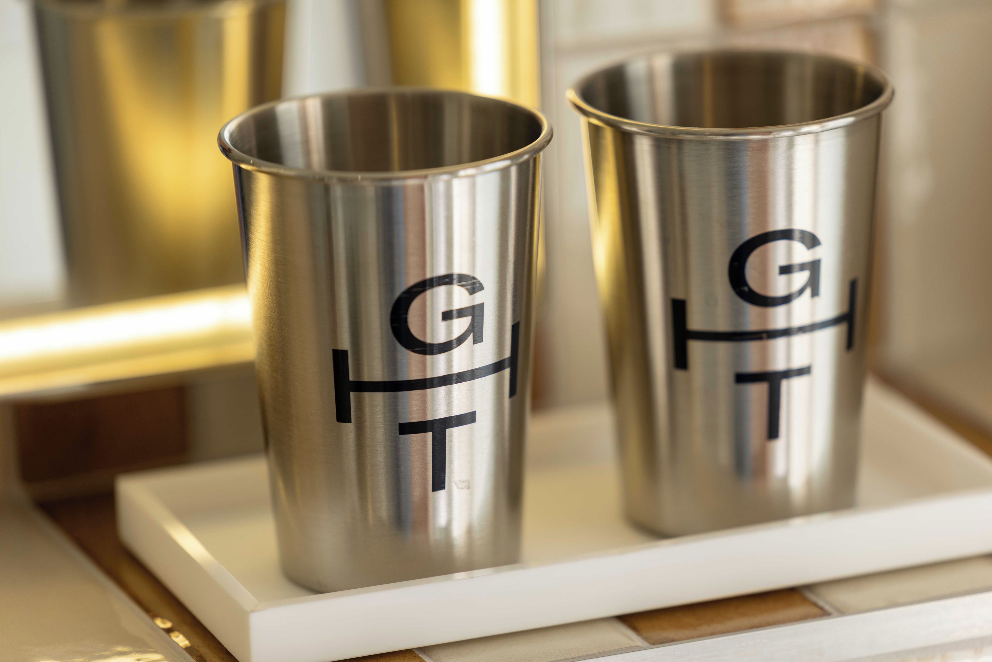 Dos vasos de acero inoxidable con las letras 'GFT' sobre una bandeja blanca.