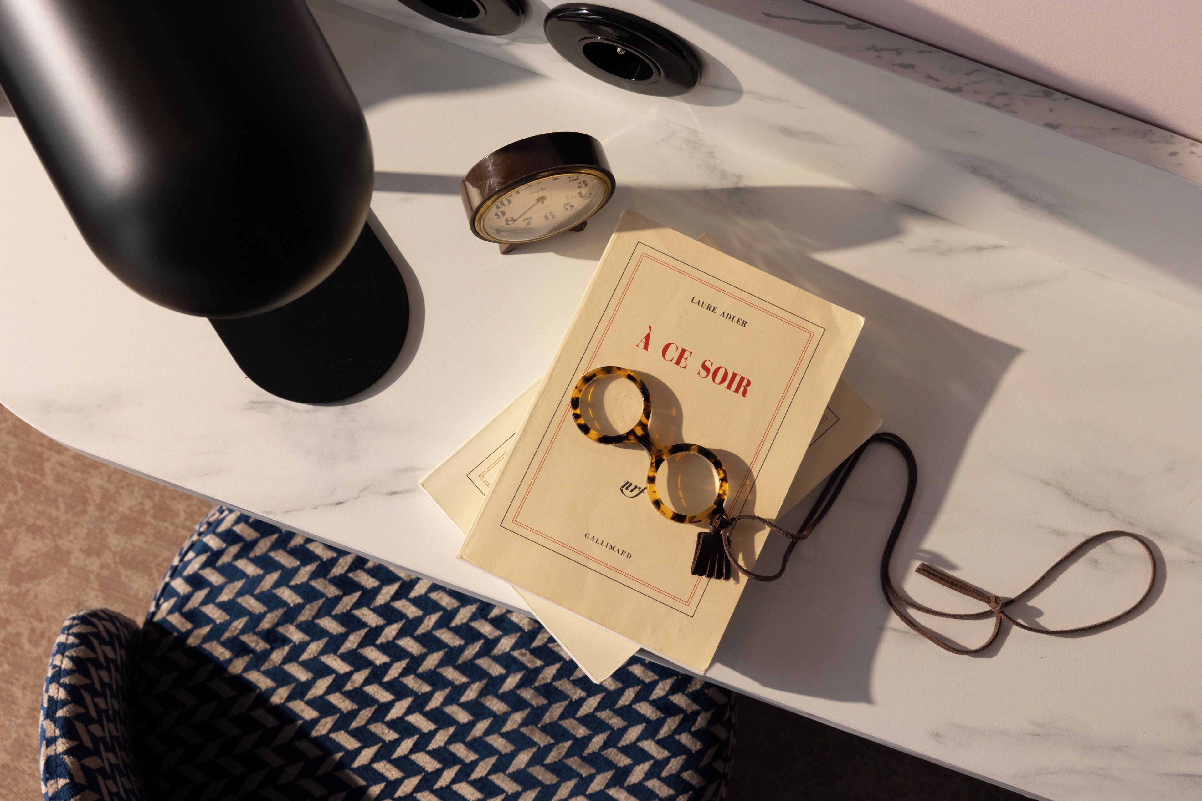 Una mesa de mármol con un libro, gafas y un reloj.