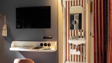 Un baño moderno con televisor montado, tocador con espejo y un perchero para toallas.