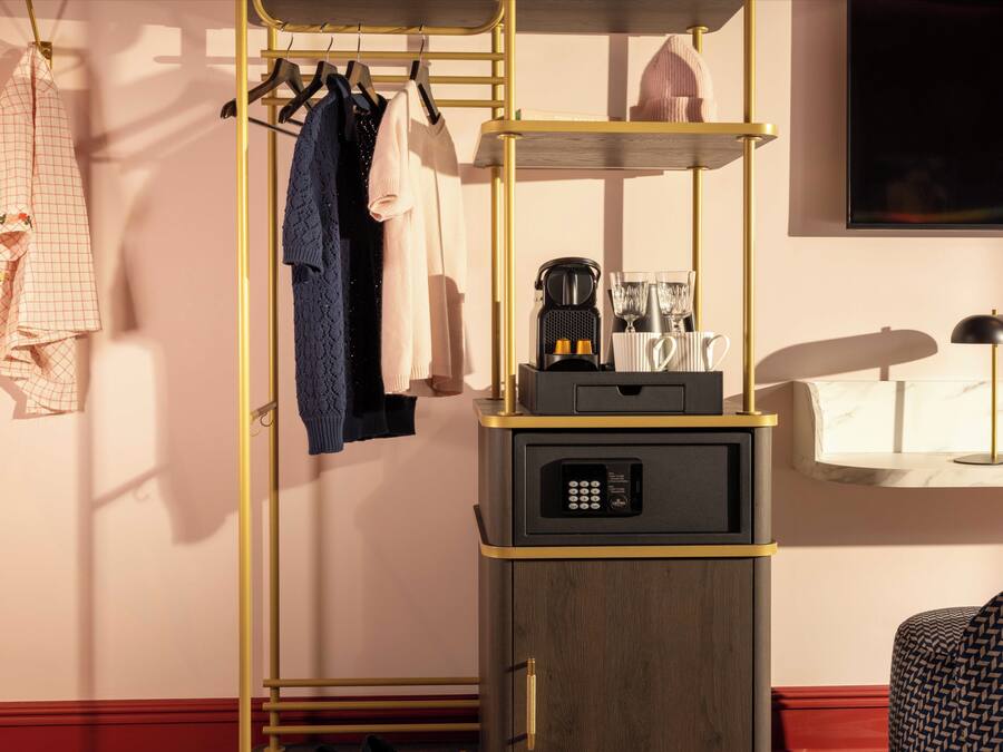 Una habitación de hotel con armario, cafetera y mesita de noche con lámpara.