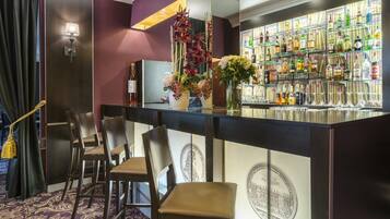 Een bar met een donker houten toonbank, meerdere stoelen en diverse flessen drank.