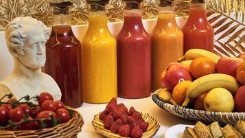 Una mesa con diferentes alimentos y bebidas, entre ellas botellas de jugo, una cesta de frutas y un tazón de fresas.