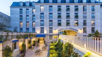 Experience the classic European charm of Hotel Le Versailles, featuring a symmetrical facade with balconies and lush greenery.