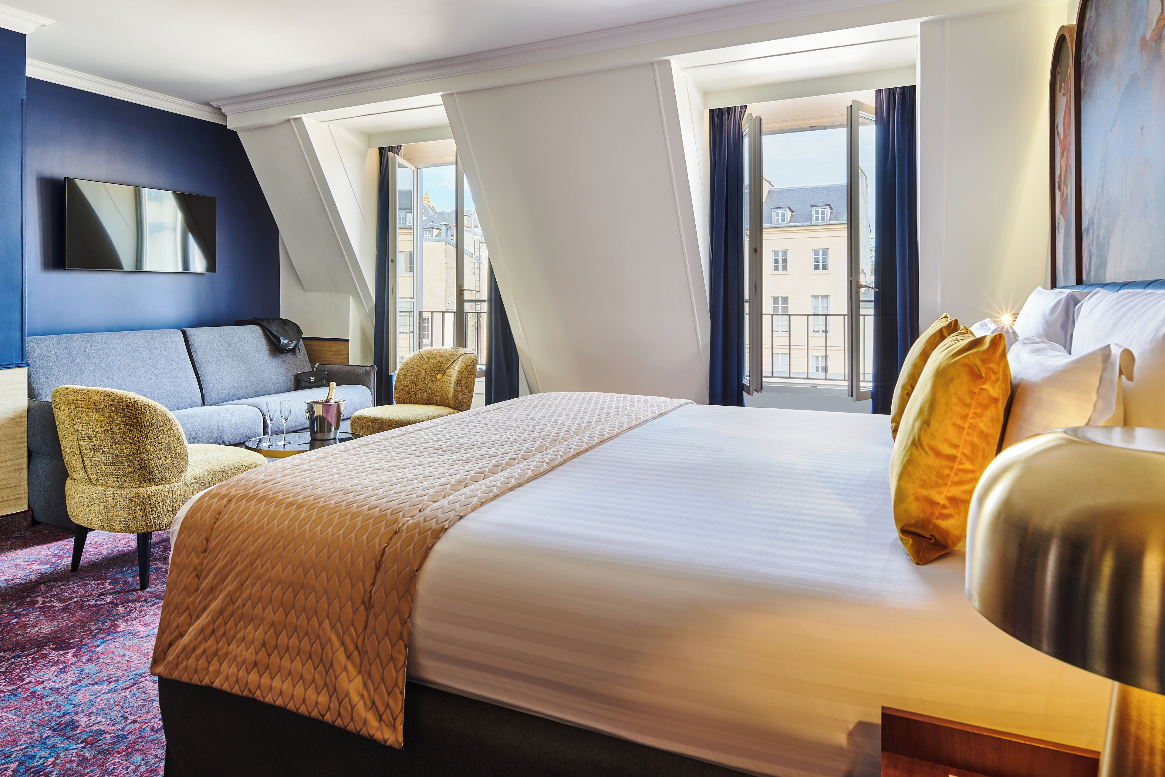 A hotel room with a large bed, a sofa, a chair, and a TV.