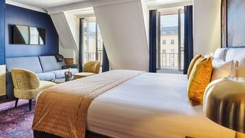 A hotel room with a large bed, a sofa, a chair, and a TV.
