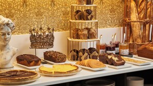 Une variété de produits de boulangerie, notamment des gâteaux, des tartes et des pâtisseries, est exposée sur une table, le tout sur fond d’un papier peint à motifs.