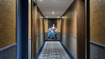 A hallway with patterned wallpaper, a blue carpet, and a painting of a woman in blue.