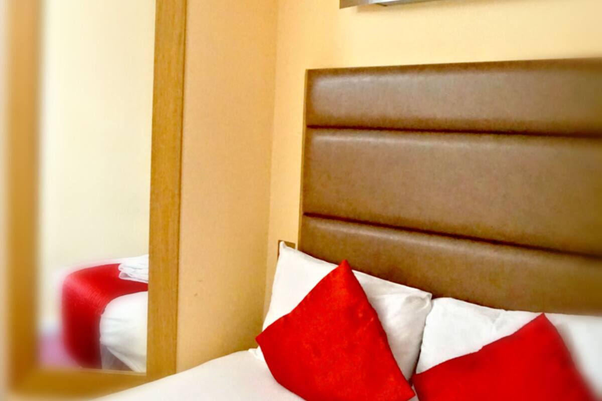 A hotel room with a bed, a mirror, and a wall-mounted light fixture.