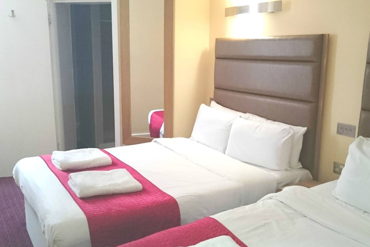 A hotel room with two beds, each with white linens and a red accent.