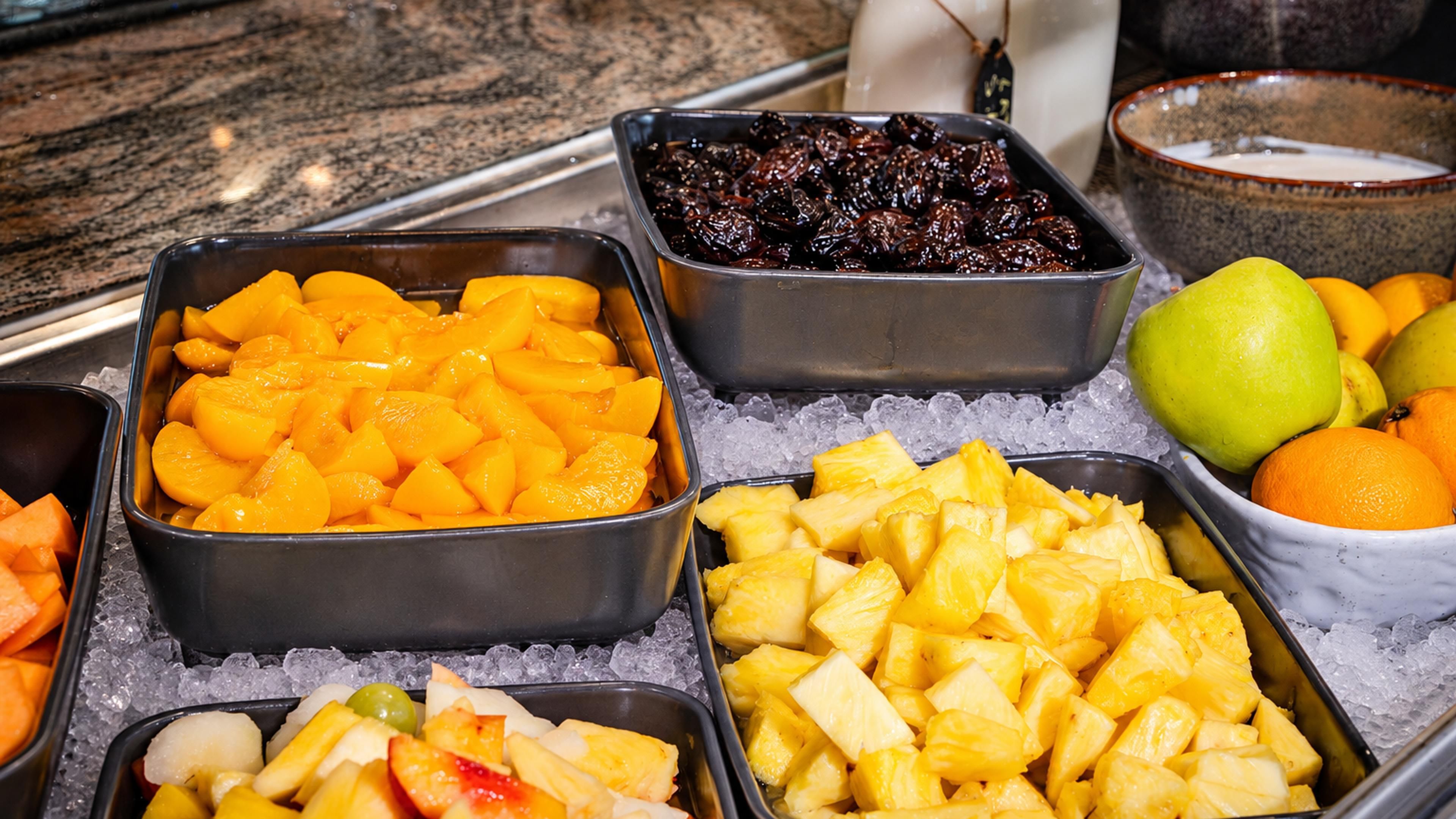 Une présentation de fruits comprenant différents types de fruits dans des récipients en métal, de la glace et un bol de yaourt.