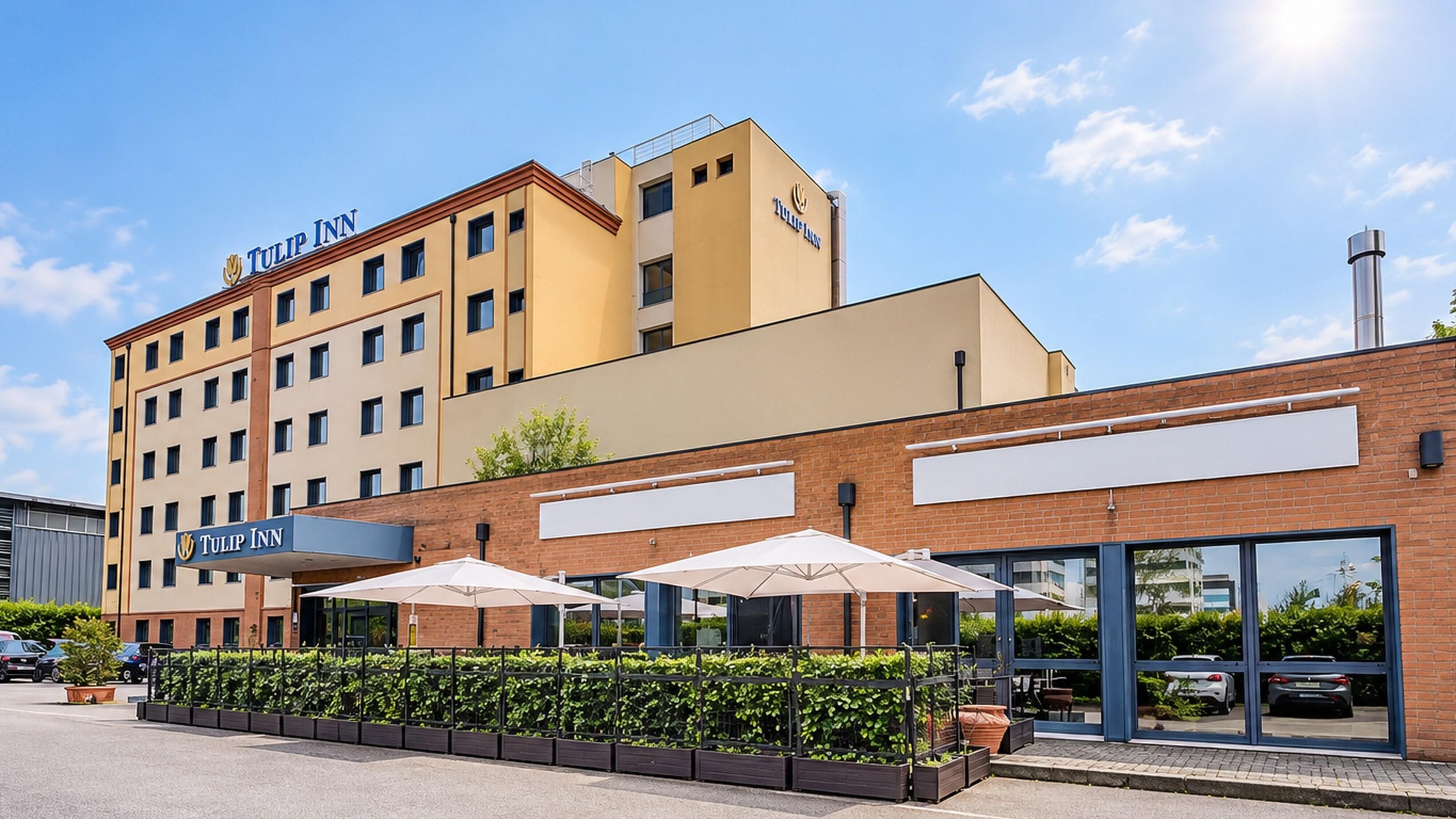 A hotel with a prominent 'Tulip Inn' sign, a brick facade, and outdoor umbrellas.