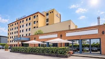 Ein Hotel mit einem gut sichtbaren 'Tulip Inn' Schild, einer Ziegel-Fassade und Sonnenschirmen.
