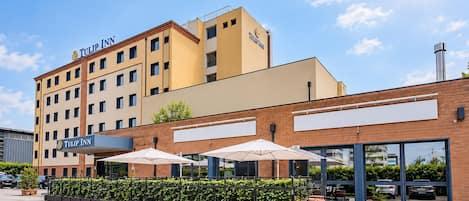Un hotel con un llamativo letrero de 'Tulip Inn', fachada de ladrillo y sombrillas exteriores.