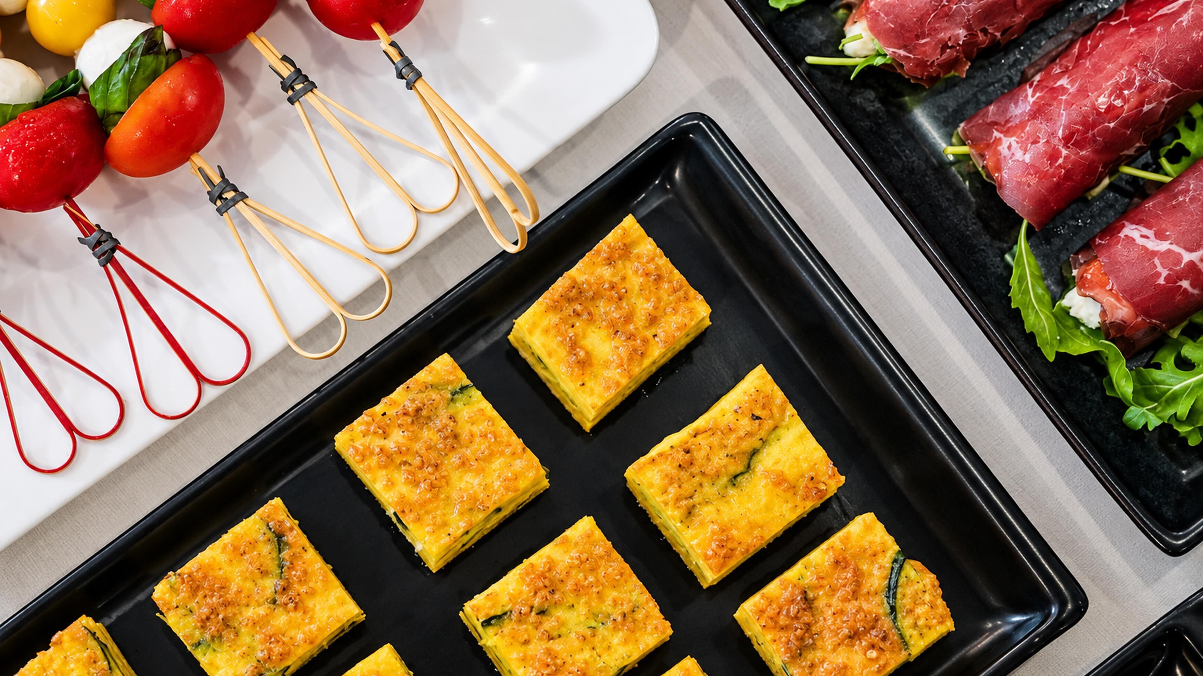 Une plaque contenant des plats cuits au four, de forme carrée et de couleur brun doré, probablement une sorte de tarte salée ou de gratin, disposés avec soin sur un plateau noir.