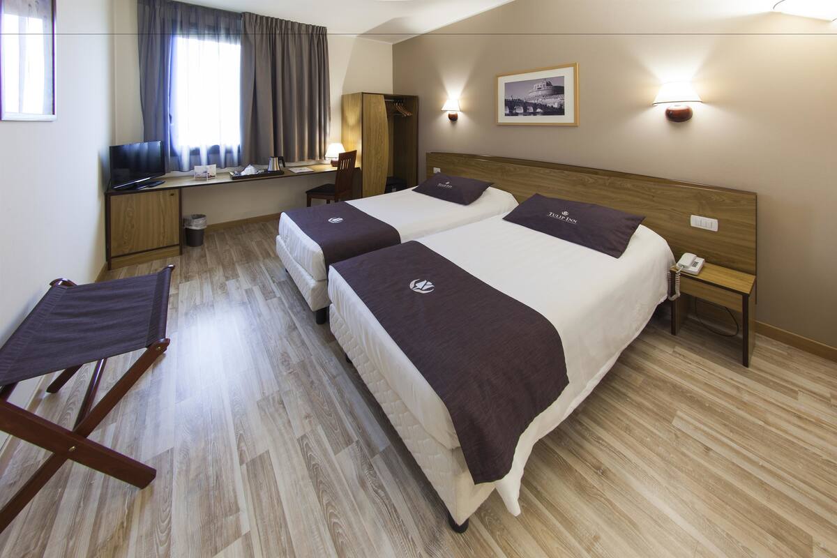 Une chambre d’hôtel avec deux lits, un bureau, une chaise et une petite table.