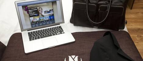 A laptop on a bed with a dark brown bag beside it.
