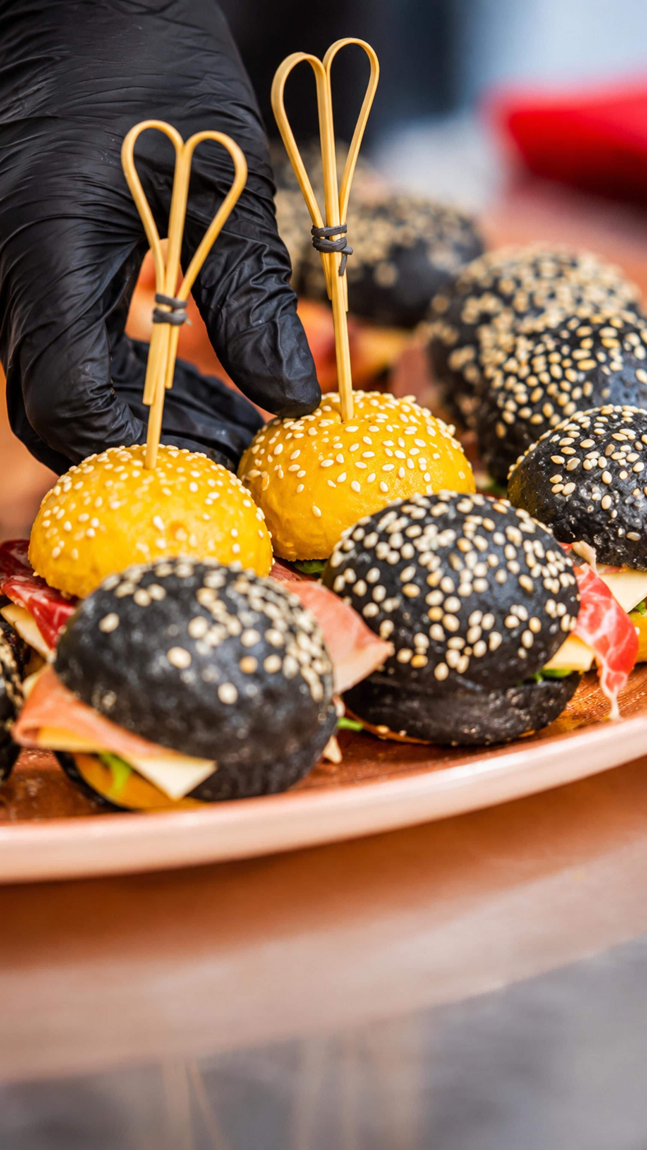A plate of food with sesame seed buns and a gloved hand holding a toothpick.