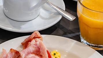 Une table dressée pour le petit-déjeuner avec une tasse de café, des croissants, du jambon, des œufs brouillés et un verre de jus d’orange.