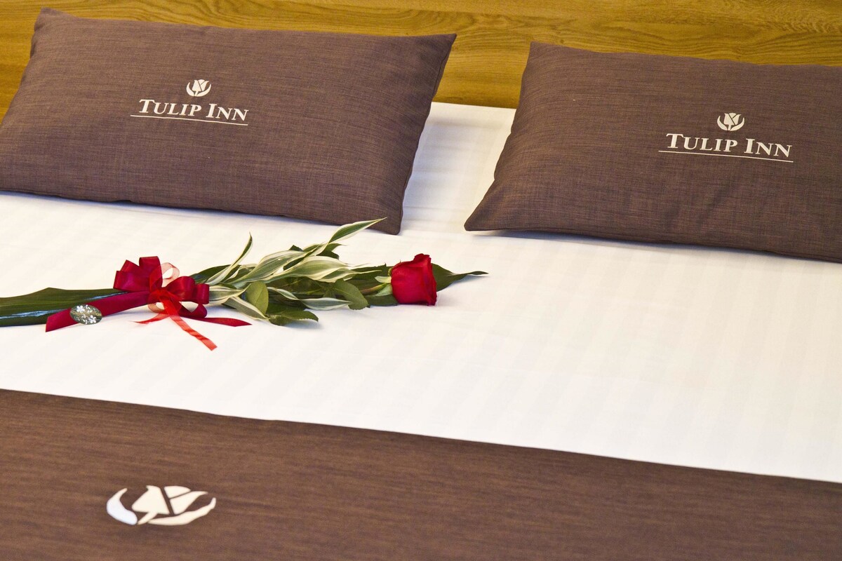 Una cama con dos almohadas que indican "Tulip Inn" y un ramo de flores con una cinta roja.