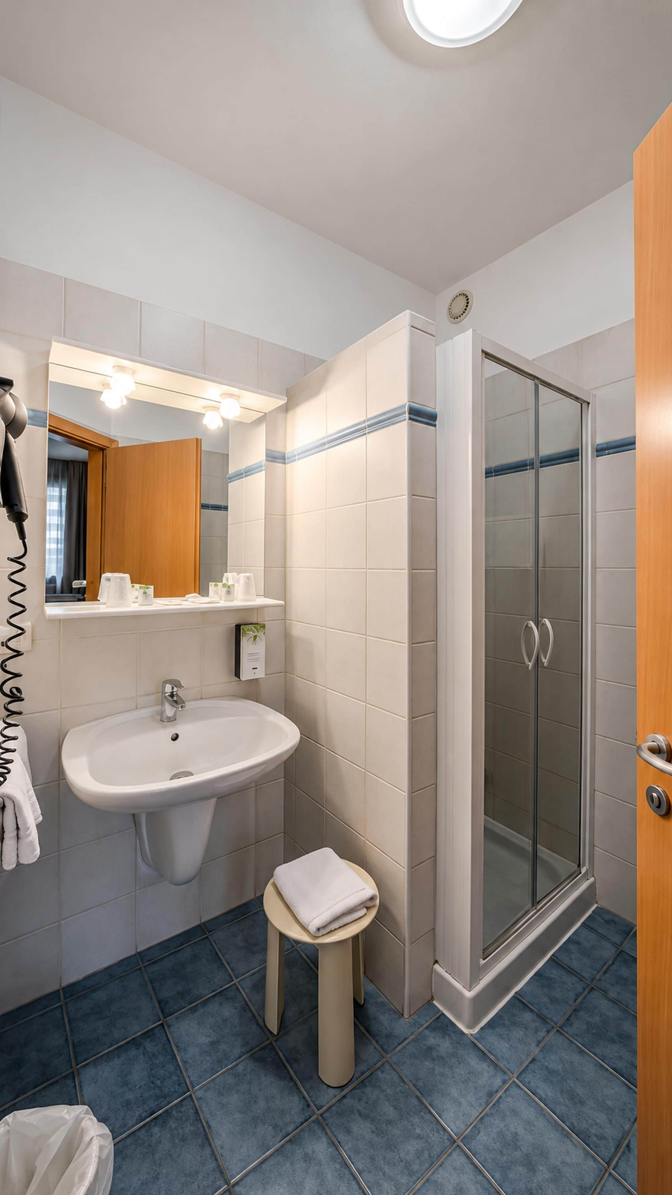Un baño con lavamanos, espejo, toallero y ducha con mampara de vidrio.
