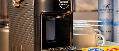 Una máquina de café sobre una mesa con una lata de agua San Benedetto y una caja de té Lipton.