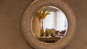 Een ronde spiegel met een geruit frame die een eethoek toont, met een tafel, stoelen en een vaas met bloemen.