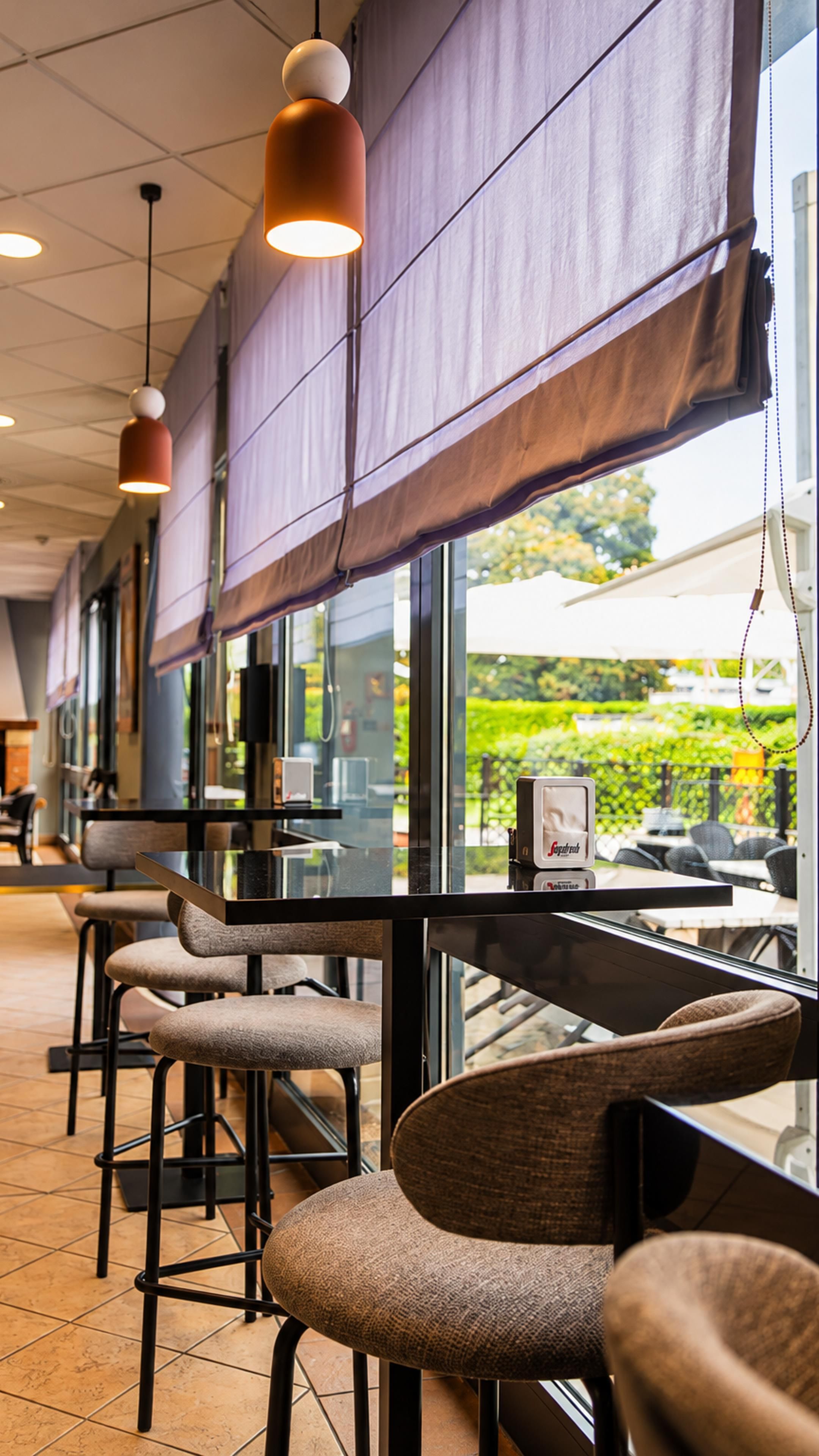 L’intérieur d’un restaurant avec des tables hautes, des chaises et des lampes suspendues.