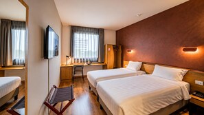 Habitación de hotel con dos camas, un escritorio, una silla, un televisor y un perchero.